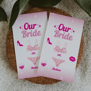 May include: Two pink cards with the text "Our Bride" in pink lettering. Each card has a pink bra and panty set, a pink high heel shoe, and a pink diamond. The bra size is 34C and the panty size is Medium.
