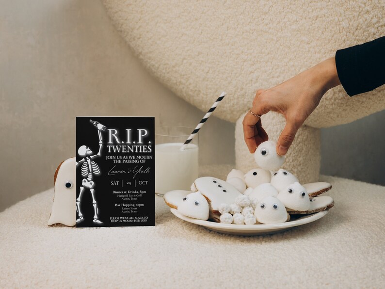 May include: A black and white invitation card with the text "R.I.P. TWENTIES" and a skeleton holding a bottle. The invitation is for a party celebrating the end of someone's twenties. The card is sitting on a table with a plate of white ghost-shaped cookies with googly eyes.