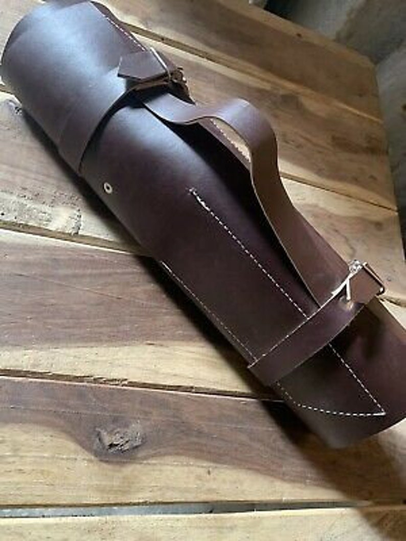 May include: A brown leather roll-up case with a strap and buckle closure. The case is made of a thick, durable leather and has a stitched design.