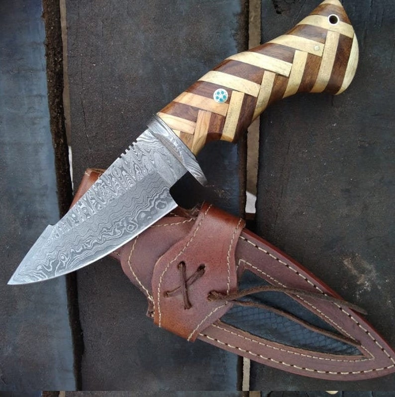 May include: A Damascus steel hunting knife with a wooden handle. The handle is made of multiple pieces of wood, creating a striped pattern. The knife is in a brown leather sheath.