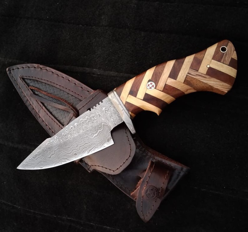 May include: A hunting knife with a patterned wooden handle and a Damascus steel blade. The knife is in a brown leather sheath.