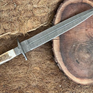 K&ouml;nnte beinhalten: Ein handgefertigtes Dolch mit einer Damaststahlklinge und einem Knochengriff. Die Klinge hat ein charakteristisches Muster und ist scharf. Der Griff ist aus Knochen und hat eine nat&uuml;rliche Oberfl&auml;che.