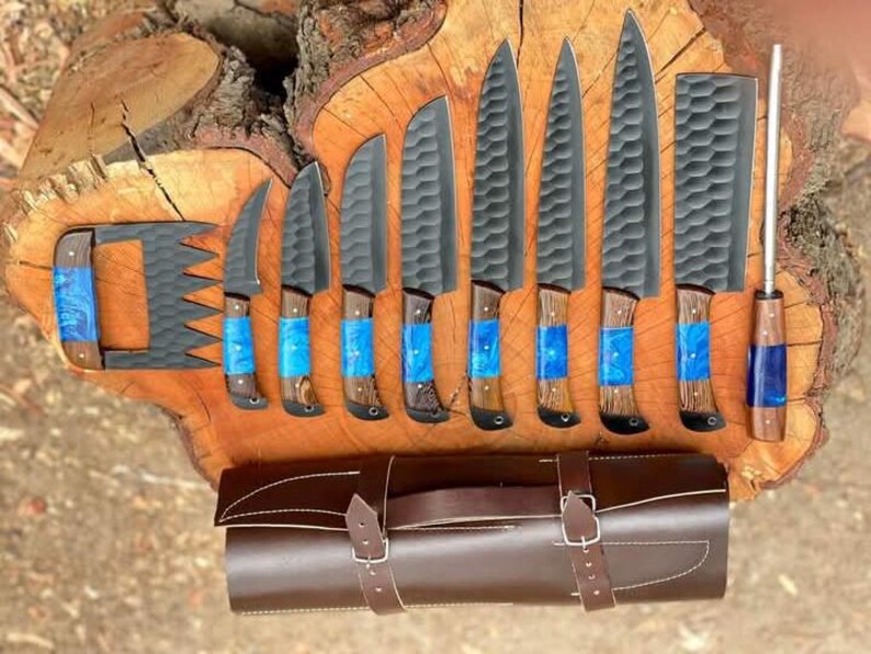 May include: A set of eight black kitchen knives with wooden handles and blue resin accents. The knives are arranged on a wooden surface with a brown leather roll-up case.