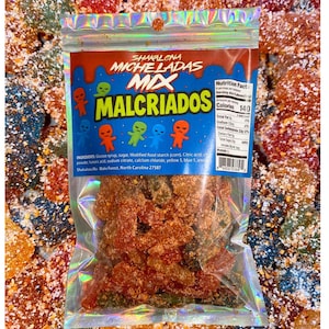 May include: A clear plastic bag filled with colorful, sugared candies. The bag features the text "Shakalona Micheladas Mix Malcriados" with alien-like characters. The background is filled with similar candies.