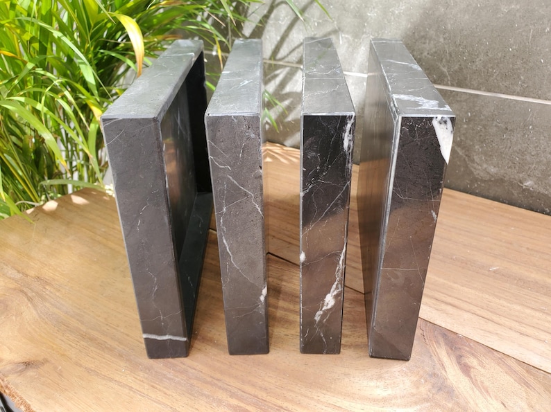 May include: Four dark gray marble bookends with white veining. The bookends are rectangular and stand upright on a wooden surface. The bookends are a decorative item for home or office.