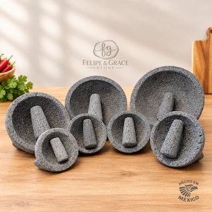 May include: A collection of six gray volcanic stone molcajetes, each featuring a matching pestle. The bowls vary in size and have a porous, textured surface. The logo Felipe & Grace Stone is visible, along with the text Hecho en México.