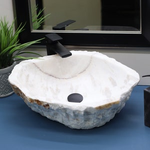 May include: A white natural stone vessel sink with a black faucet and drain stopper. The sink is on a blue countertop with a black soap dispenser.