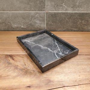 May include: A rectangular black marble tray with white veining. The tray is set on a wooden surface and has a simple, modern design. The tray is suitable for use as a decorative piece or for organizing small items.