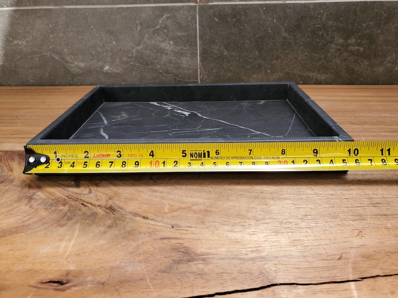 May include: A rectangular black marble tray with white veining, approximately 10 inches long. The tray is on a wooden surface, with a measuring tape alongside it.