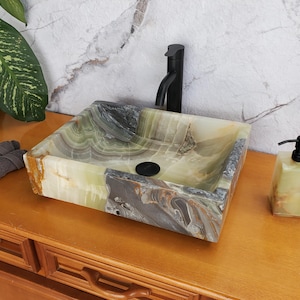 May include: A rectangular onyx stone sink with a black faucet and soap dispenser. The sink features shades of green, brown, and gray. The soap dispenser matches the sink's color scheme. A set of gray towels is on the left.