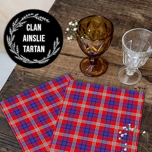 May include: Two red, blue, and white plaid tablecloths with the text "Clan Ainslie Tartan" on a black circle with white floral accents.