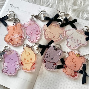 May include: A collection of colorful acrylic keychains featuring cute cartoon animal designs. Each keychain has a silver-tone heart-shaped clasp and a black ribbon. The keychains are in various colors, including orange, pink, and purple.