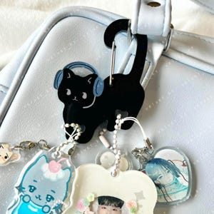 Mosquetón acrílico con forma de gato y auriculares. Ideal para guardar objetos pequeños, llaveros y tarjetas fotográficas.