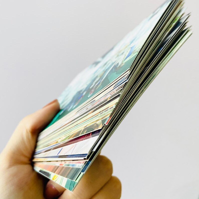 May include: A stack of colorful cards with various designs and patterns. The cards are held in a hand and are fanned out to show the different designs.