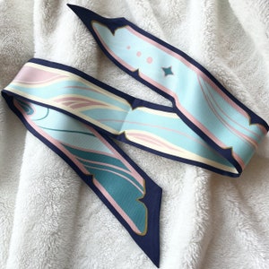 May include: A blue and pink patterned silk scarf with a navy blue trim. The scarf has a geometric design with swirls and lines.
