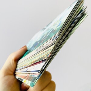 May include: A stack of colorful cards with various designs and patterns. The cards are held in a hand and are fanned out to show the different designs.