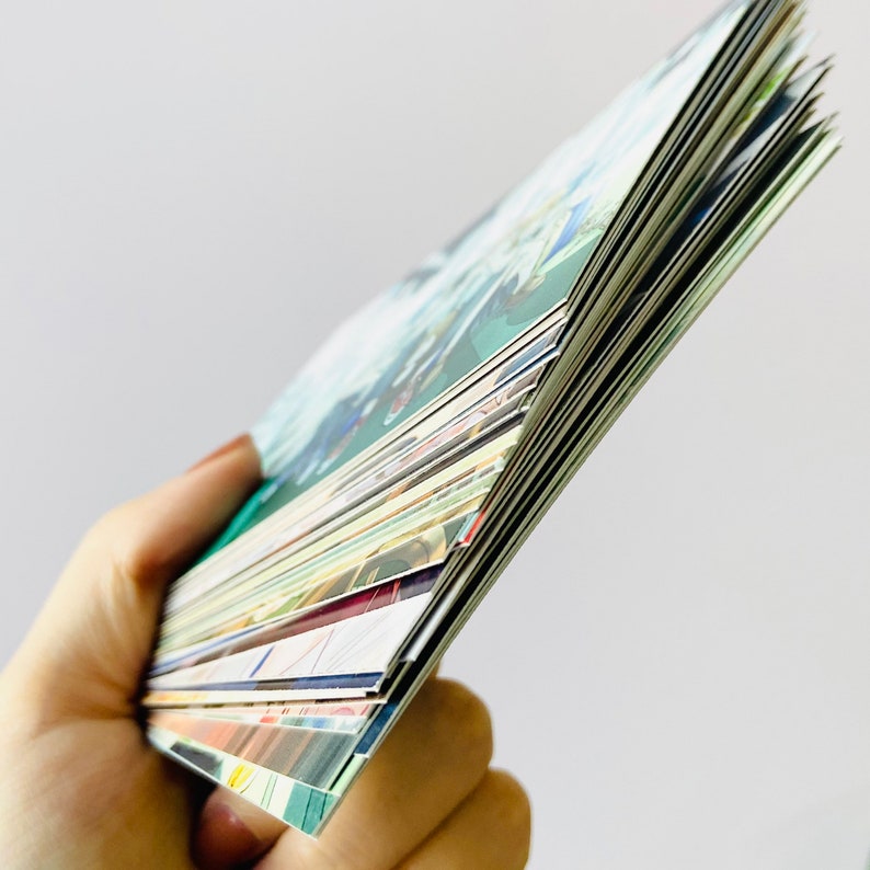 May include: A stack of colorful cards with various designs and patterns. The cards are held in a hand and are fanned out to show the different designs.