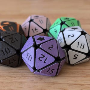May include: A collection of multi-colored, 20-sided dice for tabletop games. The dice feature a geometric design with black edges and numbered triangular faces in various colors, including purple, green, and black. The dice are arranged on a wooden surface.