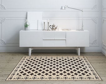 May include: A black and white geometric patterned rug with a floral border. The rug is on a wooden floor in a room with white walls and a white cabinet.