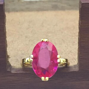 Puede incluir: Un anillo de oro con una gran piedra preciosa rosa ovalada y brillante.