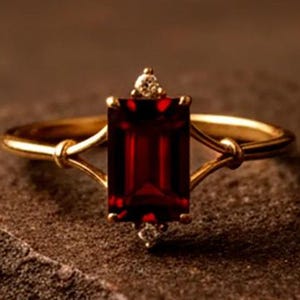 Könnte beinhalten: Ein goldener Ring mit einem rechteckigen, tiefroten Edelstein. Der Ring hat ein zartes Band mit kleinen Diamantakzenten über und unter dem Hauptstein. Die Fassung und das Band haben eine polierte Oberfläche und wirken luxuriös.