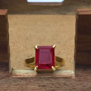 Puede incluir: Un anillo de oro con una piedra preciosa roja rectangular grande.