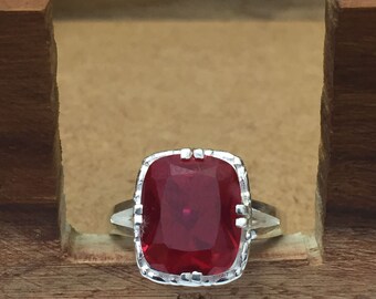 Peut inclure: Une bague en argent avec une grande pierre précieuse rouge carrée sertie dans un cadre décoratif en argent.