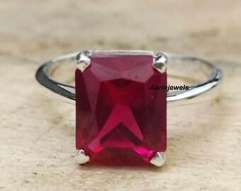Peut inclure: Une bague en argent ornée d'une grande pierre rouge foncé de forme rectangulaire. La pierre est sertie de quatre griffes, et le bracelet est lisse et poli. La bague est présentée sur une surface claire. Le texte "Aarinjewels" est visible.