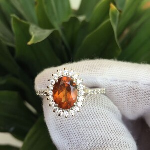 May include: A silver ring with a large oval-shaped orange gemstone surrounded by a halo of smaller white gemstones.