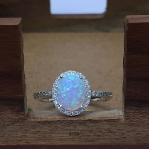 May include: A silver ring with a white opal gemstone set in a halo of smaller clear gemstones.