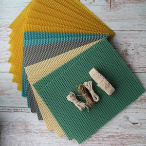May include: A stack of colorful honeycomb wax sheets in yellow, teal, gray, beige, and green. The sheets are arranged in a fan shape with a piece of lace and twine on top of the green sheet.