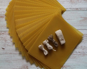 May include: A stack of yellow beeswax sheets with white and brown twine and a white lace trim on a whitewashed wooden surface.