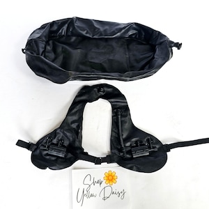 May include: Black equestrian saddle with attached straps and buckles, alongside a matching black storage bag. The saddle features a central spine and two padded sections. The image includes a handwritten sign that reads "Shop Yellow Daisy".