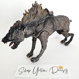 May include: A detailed, articulated figurine of a snarling, dark-colored fantasy creature with a mane and harness. The figure is posed in a dynamic stance, with its mouth open, revealing teeth. The base of the image has the text "Shop Yellow Daisy".