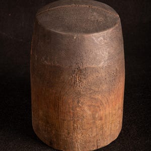 Könnte beinhalten: Zylindrisches Holzobjekt mit flacher Oberseite und leicht breiterer Basis. Das Holz hat eine natürliche Maserung und einen Farbverlauf von Dunkelbraun oben bis zu einem helleren Braun an der Basis.