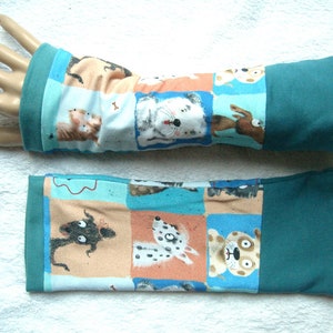 Może przedstawiać: Para ciepłych rękawiczek w kolorze turkusowym z kolorowym wzorem psów i kotów. Ciepłe rękawiczki wykonane są z miękkiej, elastycznej tkaniny.