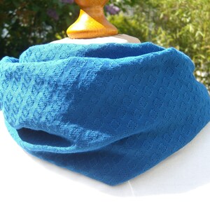 May include: A blue knitted neck warmer with a textured pattern. The neck warmer is folded and displayed on a white surface.