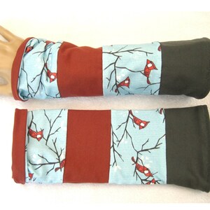 Könnte beinhalten: Ein Paar Armwärmer mit einem blauen und weißen Wintermotiv mit roten Kardinälen. Die Armwärmer haben oben einen braunen und unten einen schwarzen Bund.