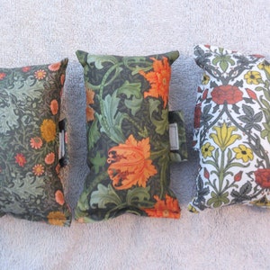 May include: Three small decorative cushions with floral patterns. The cushions are made of fabric and have a green, orange, and white colour scheme.