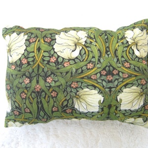 Könnte beinhalten: Ein rechteckiges Kissen mit einem floralen Muster in Grün und Weiß. Das Kissen zeigt ein sich wiederholendes Muster aus weißen Blüten und grünen Blättern auf einem dunkelgrünen Hintergrund.