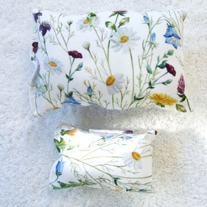 Könnte beinhalten: Zwei weiße Kissenbezüge mit einem Blumenmuster mit weißen Gänseblümchen, grünen Blättern und lila, blauen und gelben Blumen.