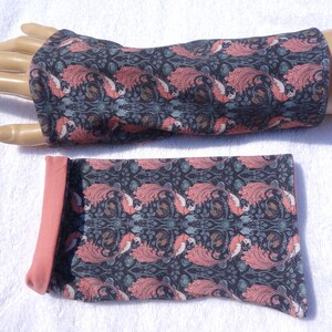May include: A pair of black and pink patterned arm warmers with a coral pink fold-over cuff. The arm warmers are made of a soft, stretchy fabric.
