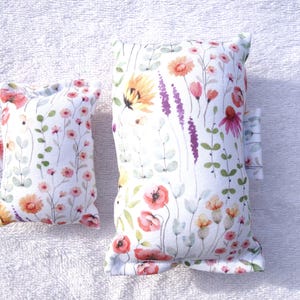 Könnte beinhalten: Zwei Kissen mit Blumenmuster. Die Kissen haben einen weißen Hintergrund mit einem farbenfrohen Druck von Blumen in Rosa-, Orange-, Lila- und Grüntönen. Die Kissen sind rechteckig und scheinen aus Stoff zu sein.