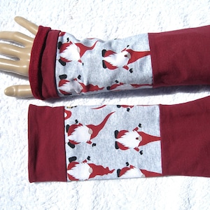 May include: A pair of red and gray arm warmers with a pattern of gnomes. The arm warmers are made of a soft, stretchy fabric and have a red cuff.