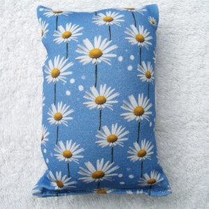 Könnte beinhalten: Ein blaues Stoffkissen mit einem weißen Gänseblümchenmuster. Das Kissen ist mit einem weichen Material gefüllt und perfekt, um jedem Raum einen Hauch von Verspieltheit zu verleihen.
