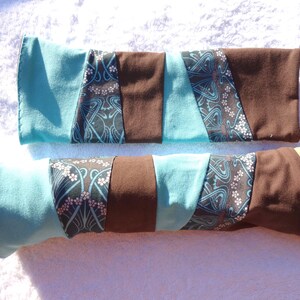 Könnte beinhalten: Zwei Armstulpen mit Patchwork-Design. Die Stulpen haben Abschnitte aus türkisem, braunem und gemustertem Stoff mit einem floralen Design. Eine Stulpe befindet sich auf einer Mannequin-Hand.