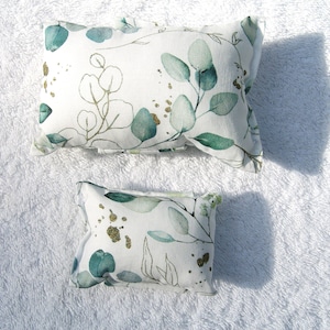 Könnte beinhalten: Zwei Dekokissen mit weißem Hintergrund und einem grünen und goldenen Blumenmuster. Das größere Kissen ist rechteckig und das kleinere Kissen ist quadratisch.