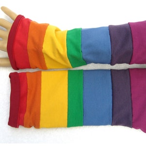 Könnte beinhalten: Ein Paar Regenbogen-gestreifte Armwärmer mit roten, orangen, gelben, grünen, blauen, violetten und burgunderfarbenen Streifen. Die Armwärmer sind aus einem weichen, dehnbaren Stoff gefertigt und perfekt, um Ihre Arme in den kühleren Monaten warm zu halten.