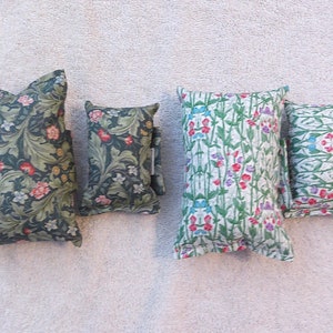 Könnte beinhalten: Vier dekorative Kissen mit Blumenmustern. Die Kissen sind in verschiedenen Größen und mit unterschiedlichen Blumendesigns. Die Kissen sind grün, weiß und rosa.