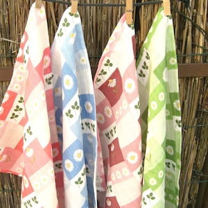 Könnte beinhalten: Vier Geschirrtücher hängen an einer Wäscheleine. Die Tücher sind aus weißem Stoff mit einem karierten Muster und haben ein Blumendesign mit rosa, roten, blauen und grünen Akzenten.